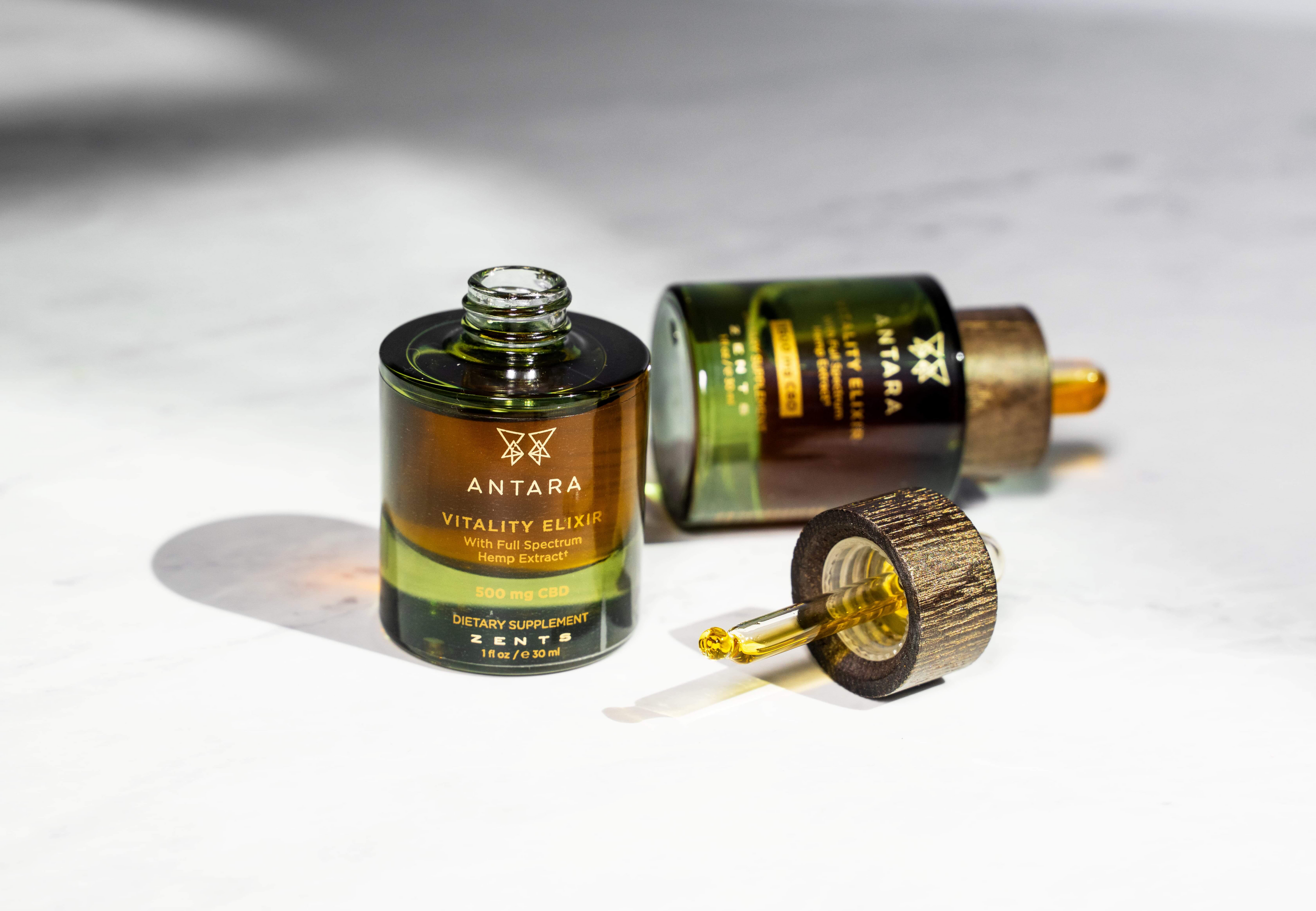 Two bottles of Antara Vitality elixir on a white surface with one dropper laying on its side