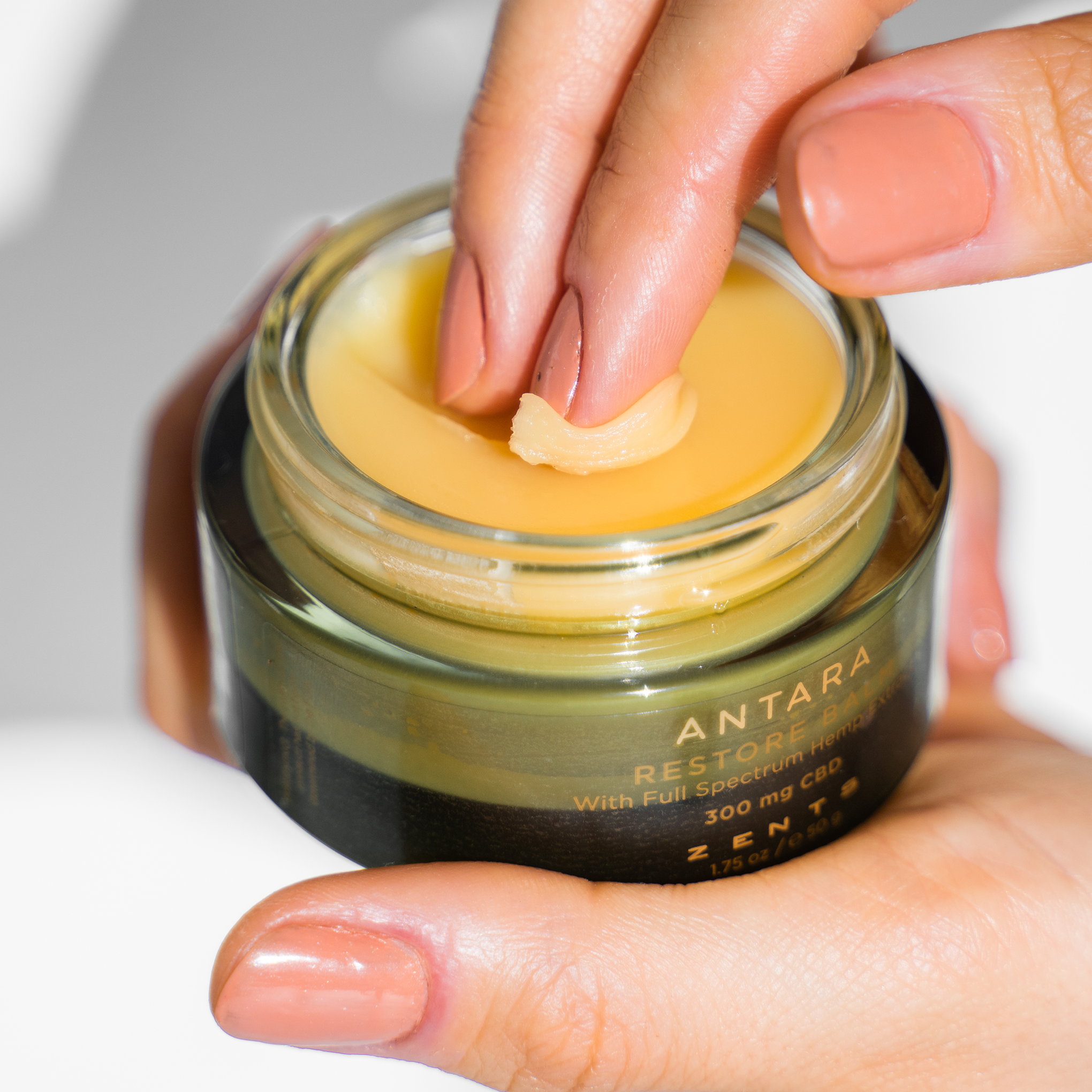 Woman smoothing fingers across open jar of Restore Balm 300 mg