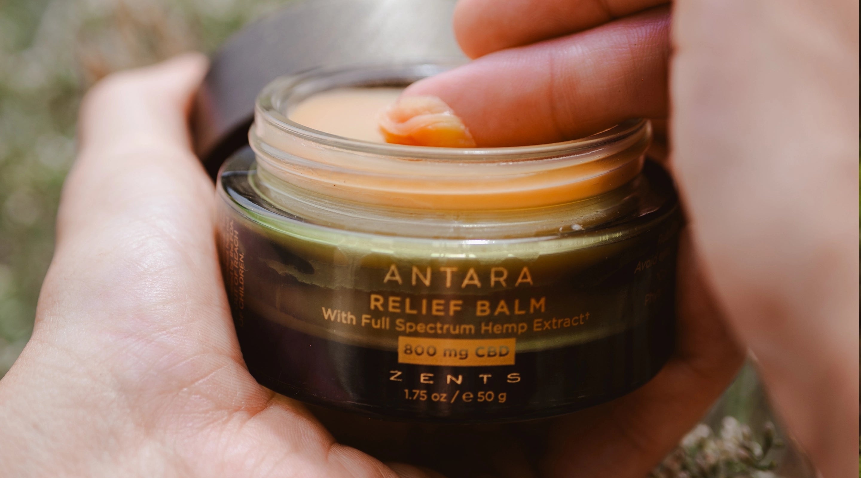 Jar of Antara Relief Balm with a person dipping a finger in