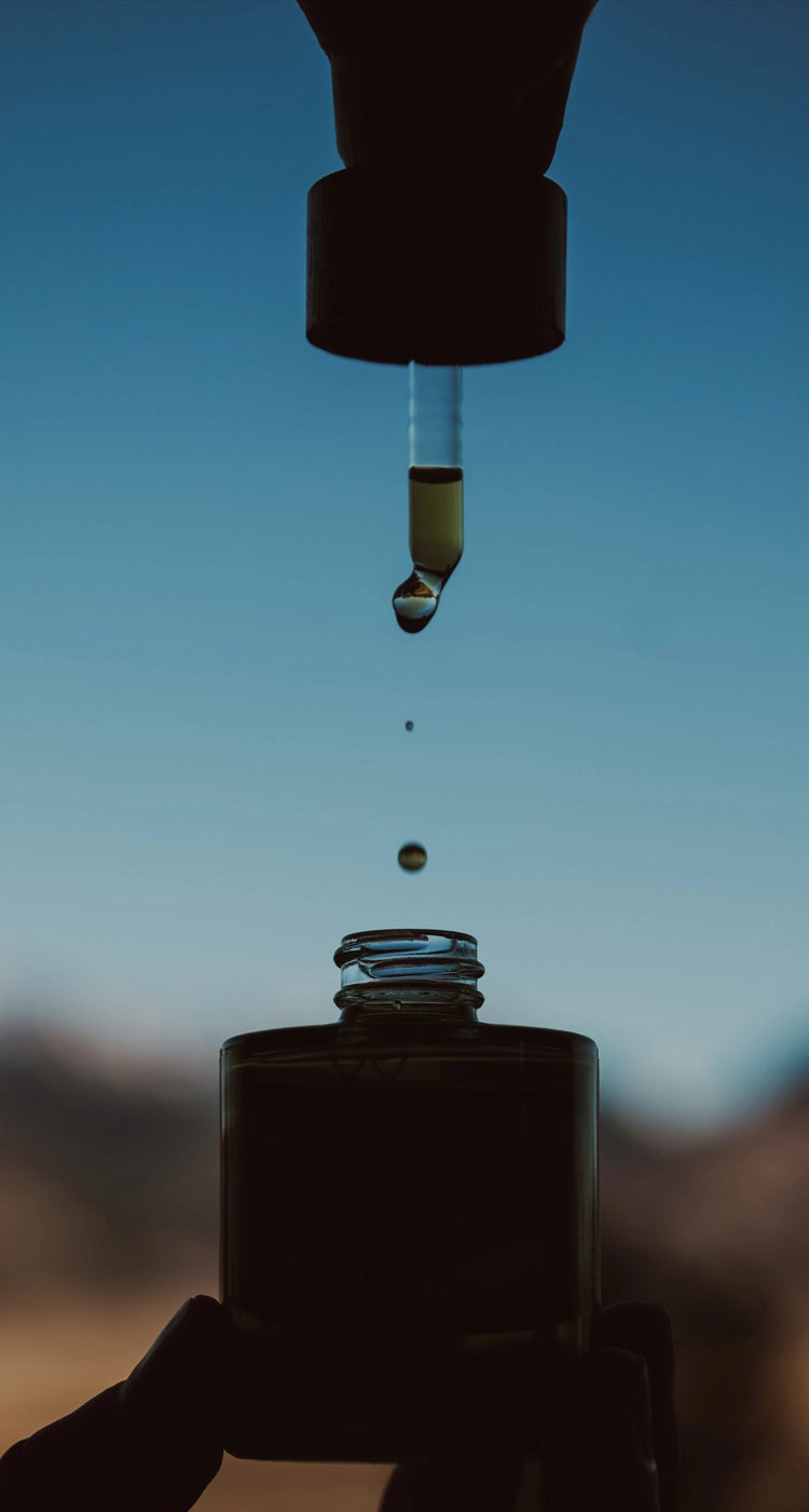 A dropper of Vitality Elixir dripping into the jar with a bright blue natural blurred background. 