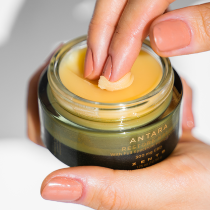 Woman smoothing fingers across open jar of Restore Balm 300 mg 